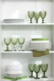 Photo of Clean glasses and plates on shelves indoors