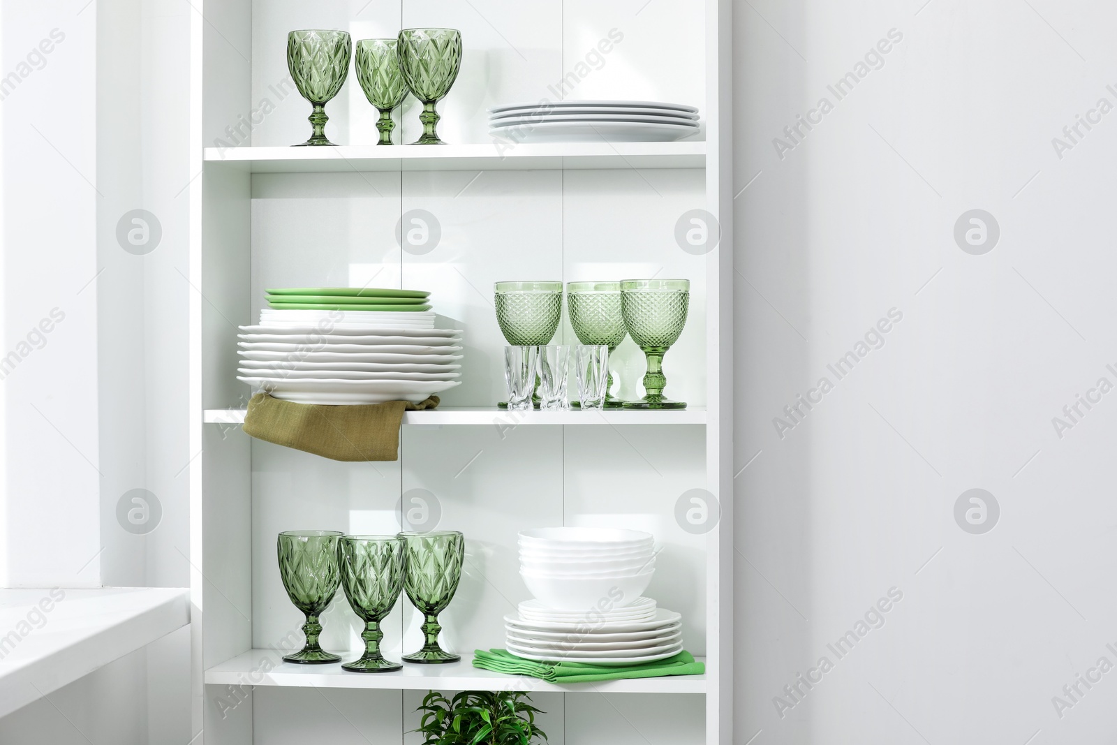 Clean glasses and plates on shelves near white wall indoors, space for text Photo of Clean glasses and plates on shelves near white wall indoors, space for text