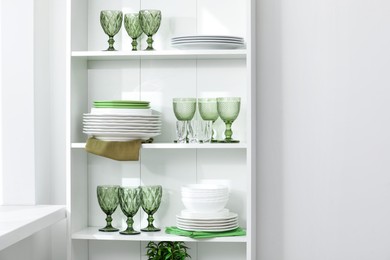 Photo of Clean glasses and plates on shelves near white wall indoors, space for text