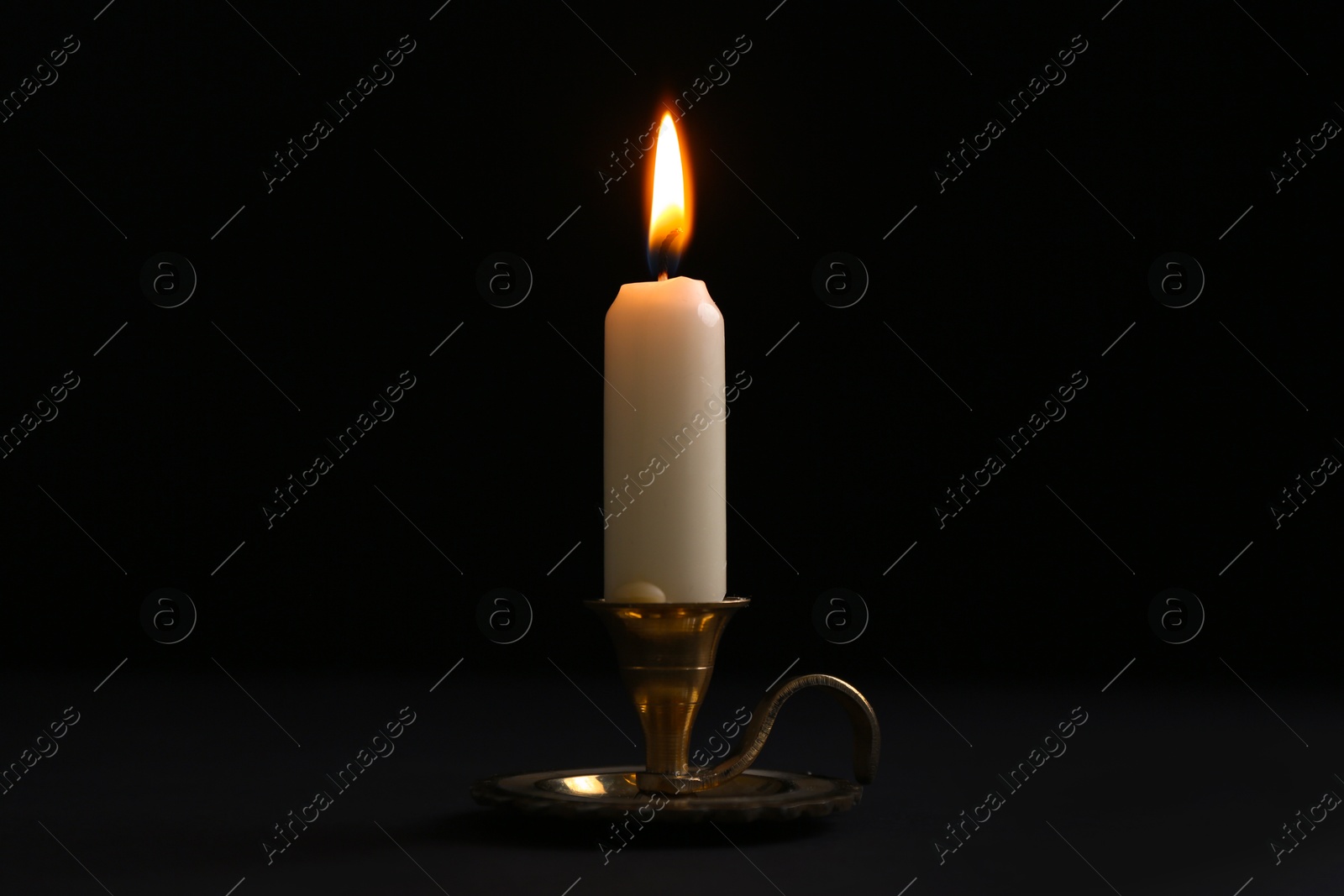 Photo of Burning candle in candlestick on black background