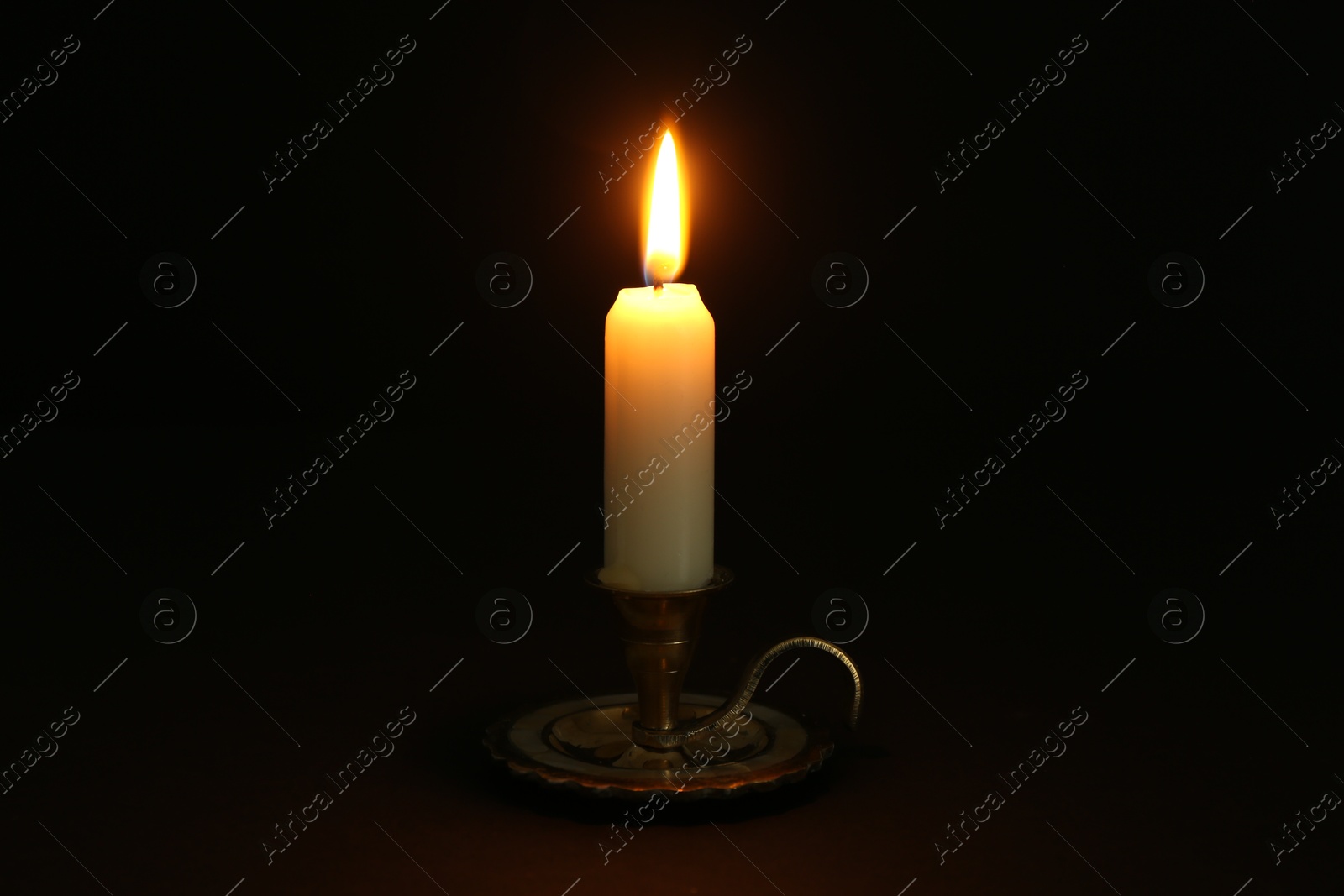 Photo of Burning candle in candlestick on black background