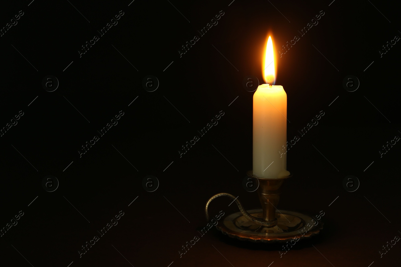 Photo of Burning candle in candlestick on black background, space for text