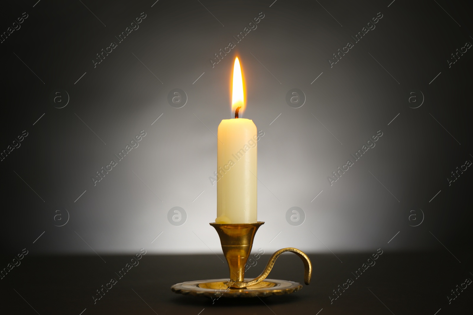 Burning candle in candlestick on black table against light background Photo of Burning candle in candlestick on black table against light background