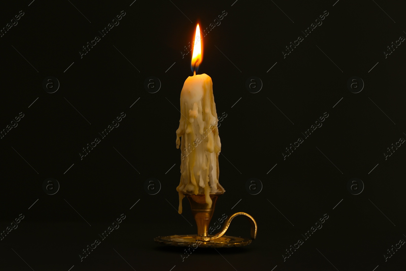 Burning candle in candlestick on black background Photo of Burning candle in candlestick on black background