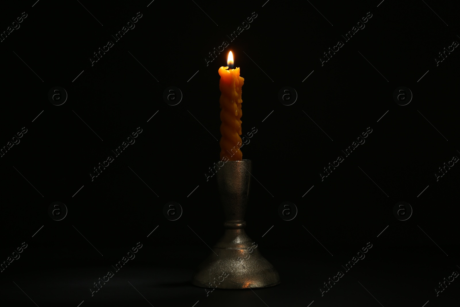 Burning candle in candlestick on black background Photo of Burning candle in candlestick on black background
