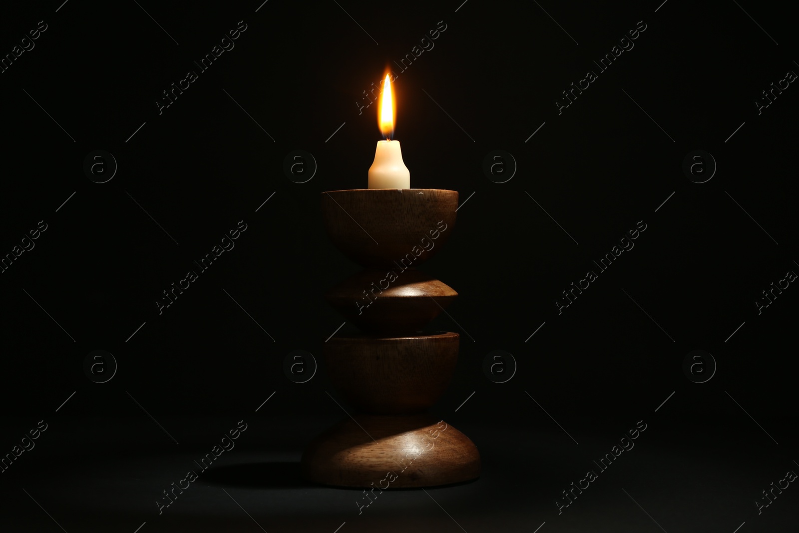 Photo of Burning candle in candlestick on black background