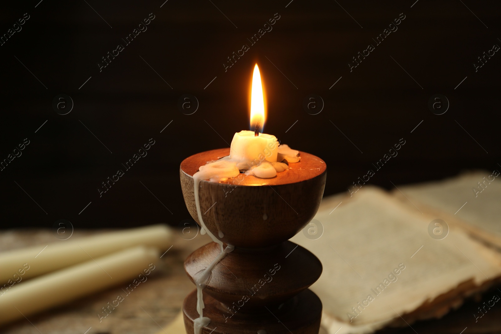 Burning candle in candlestick and old book on table, closeup Photo of Burning candle in candlestick and old book on table, closeup