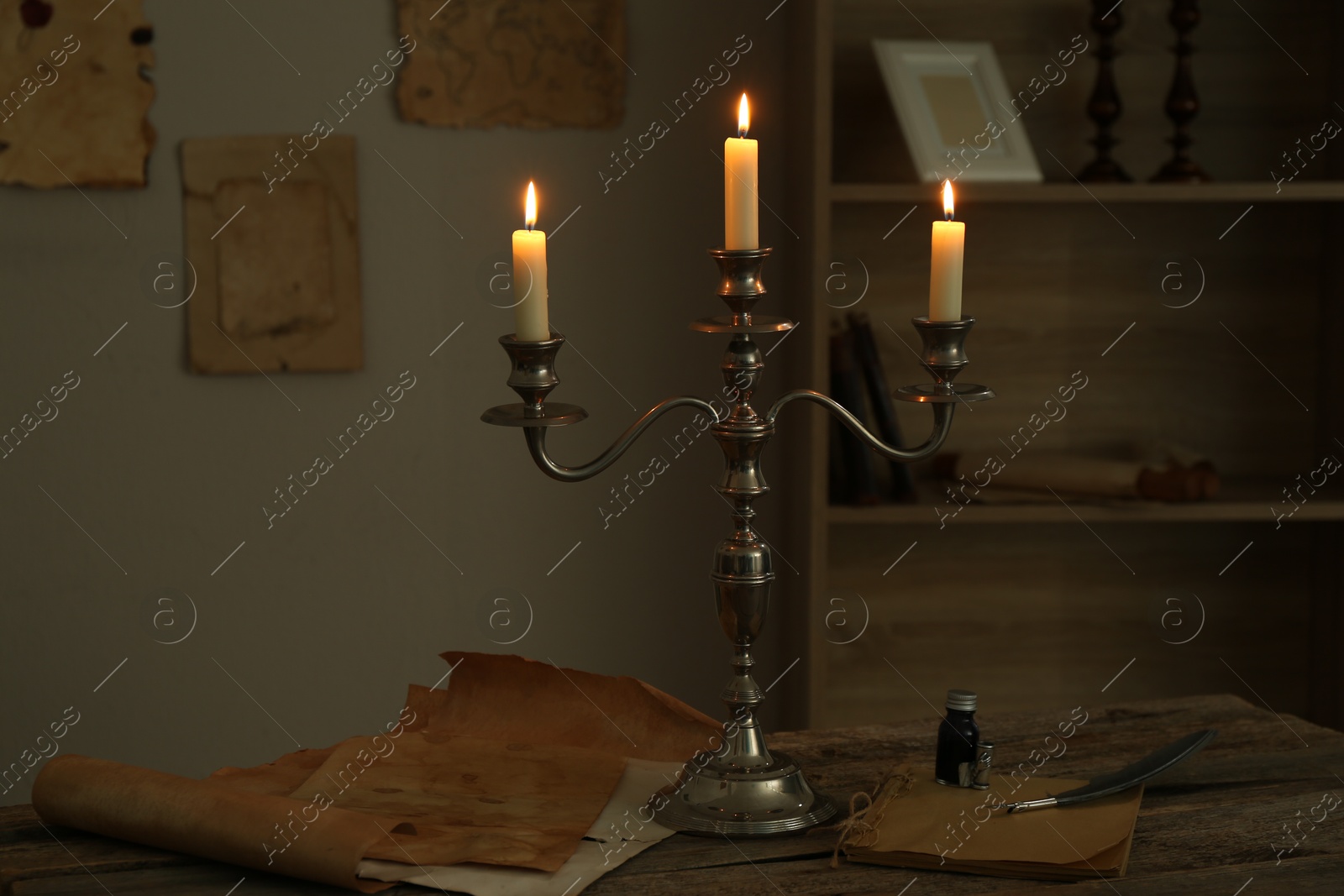 Burning candles in candlestick, vintage papers, inkwell and feather on wooden table indoors Photo of Burning candles in candlestick, vintage papers, inkwell and feather on wooden table indoors