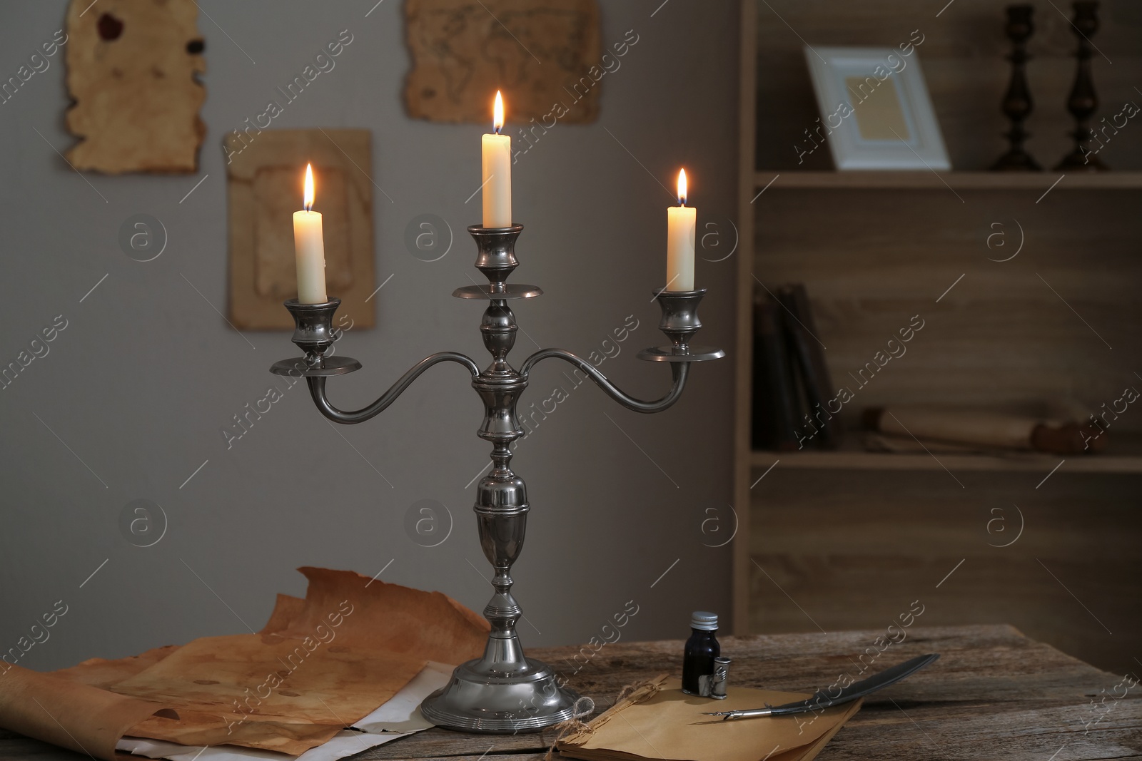 Burning candles in candlestick, vintage papers, inkwell and feather on wooden table indoors Photo of Burning candles in candlestick, vintage papers, inkwell and feather on wooden table indoors