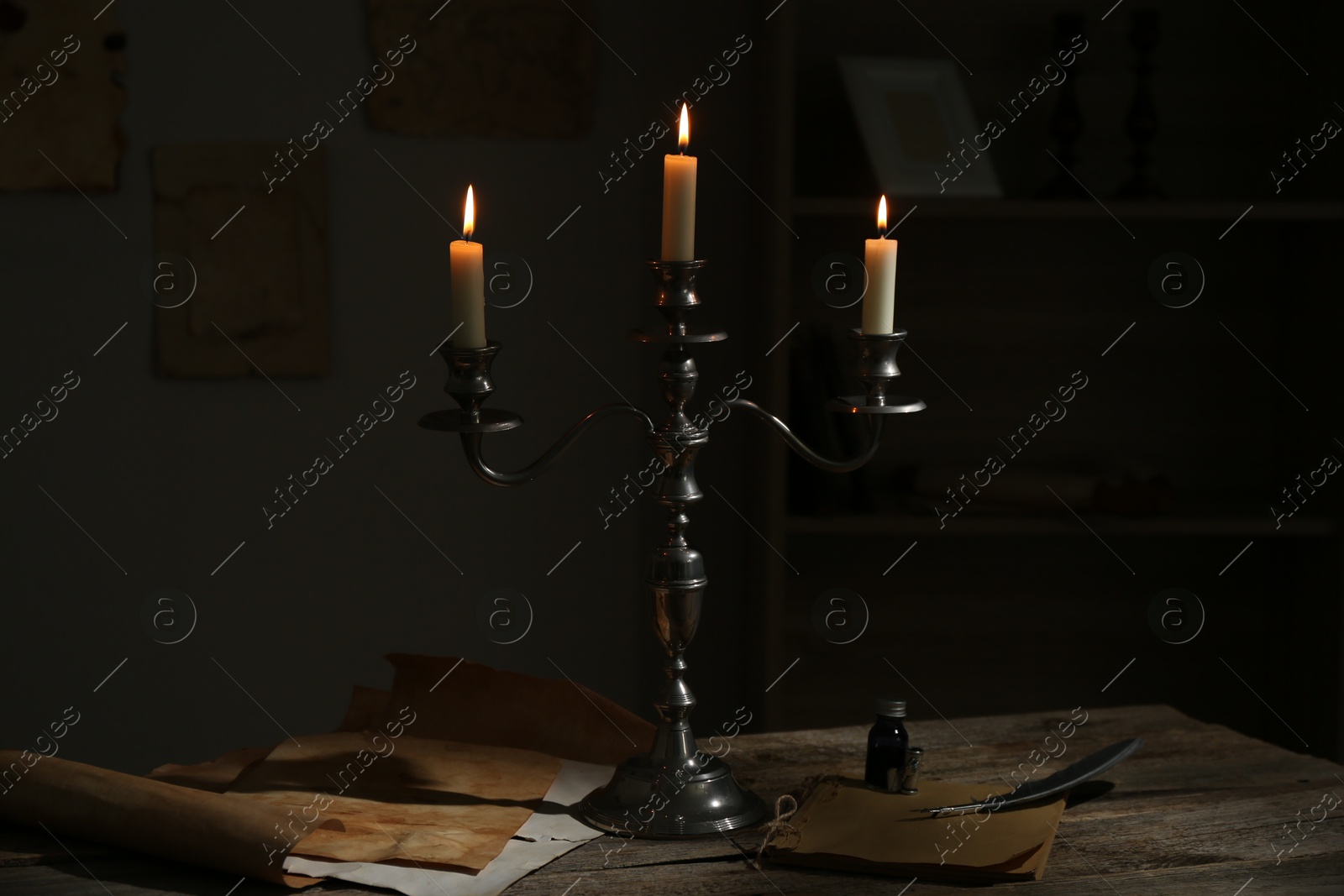 Burning candles in candlestick, vintage papers, inkwell and feather on wooden table indoors Photo of Burning candles in candlestick, vintage papers, inkwell and feather on wooden table indoors