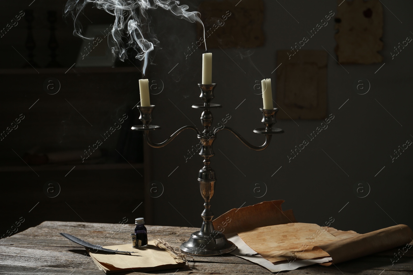 Smoldering candles in candlestick, vintage papers, inkwell and feather on wooden table indoors Photo of Smoldering candles in candlestick, vintage papers, inkwell and feather on wooden table indoors