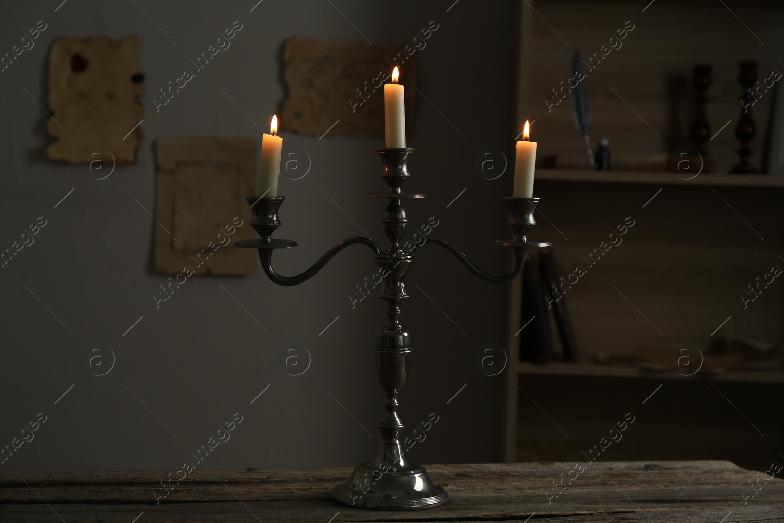 Burning candles in candlestick on wooden table indoors Photo of Burning candles in candlestick on wooden table indoors