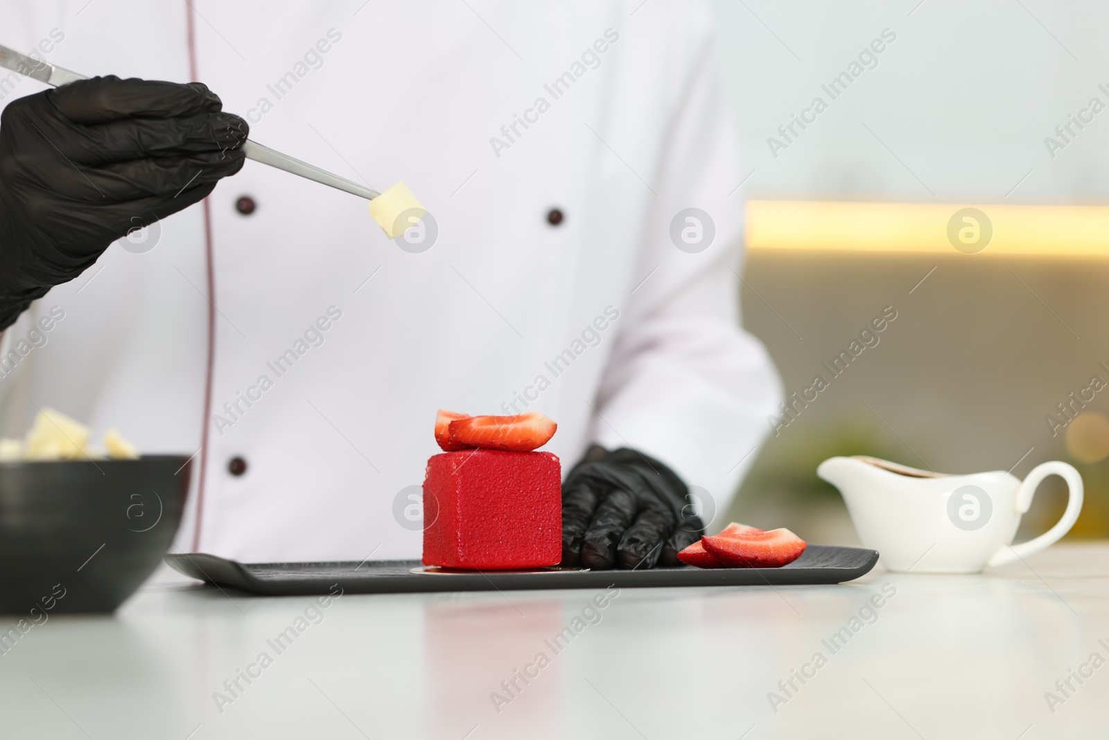 Confectioner decorating tasty dessert at white table in kitchen, closeup Photo of Confectioner decorating tasty dessert at white table in kitchen, closeup