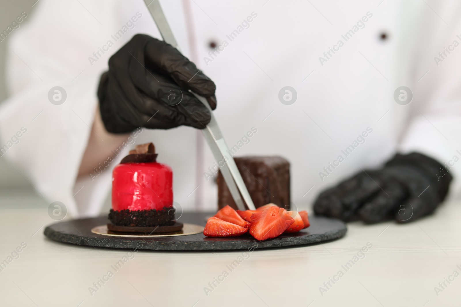 Confectioner decorating tasty dessert with strawberries at white wooden table in kitchen, selective focus Photo of Confectioner decorating tasty dessert with strawberries at white wooden table in kitchen, selective focus