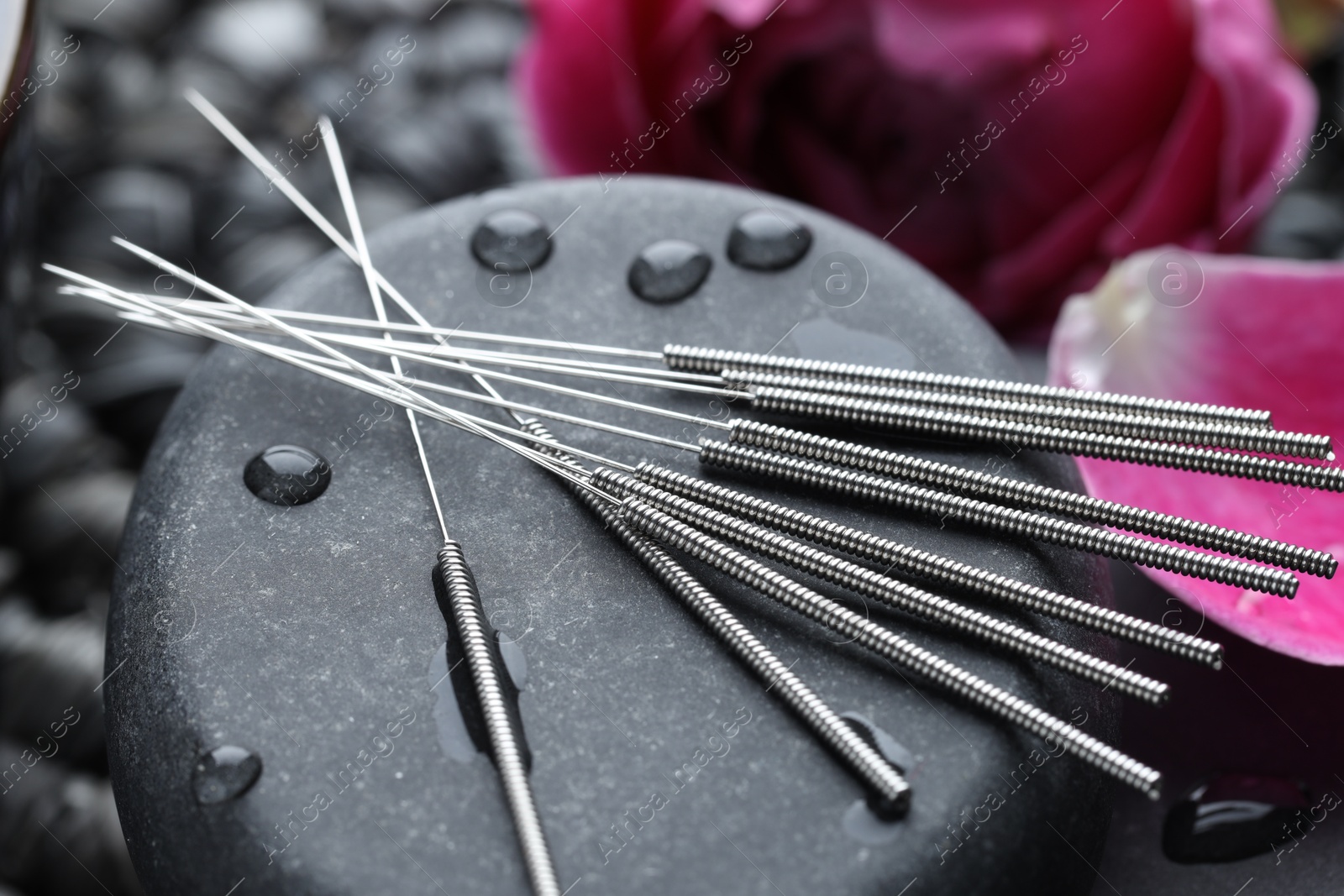 Acupuncture needles, wet spa stone and flowers on wicker mat, closeup Photo of Acupuncture needles, wet spa stone and flowers on wicker mat, closeup