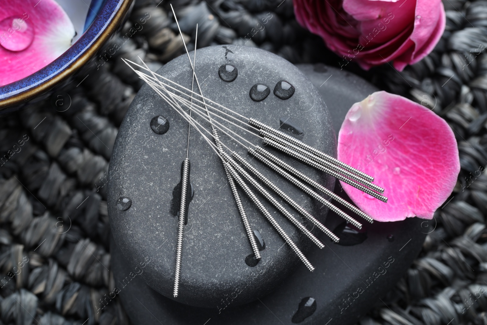 Acupuncture needles, wet spa stones and flowers on wicker mat, flat lay Photo of Acupuncture needles, wet spa stones and flowers on wicker mat, flat lay