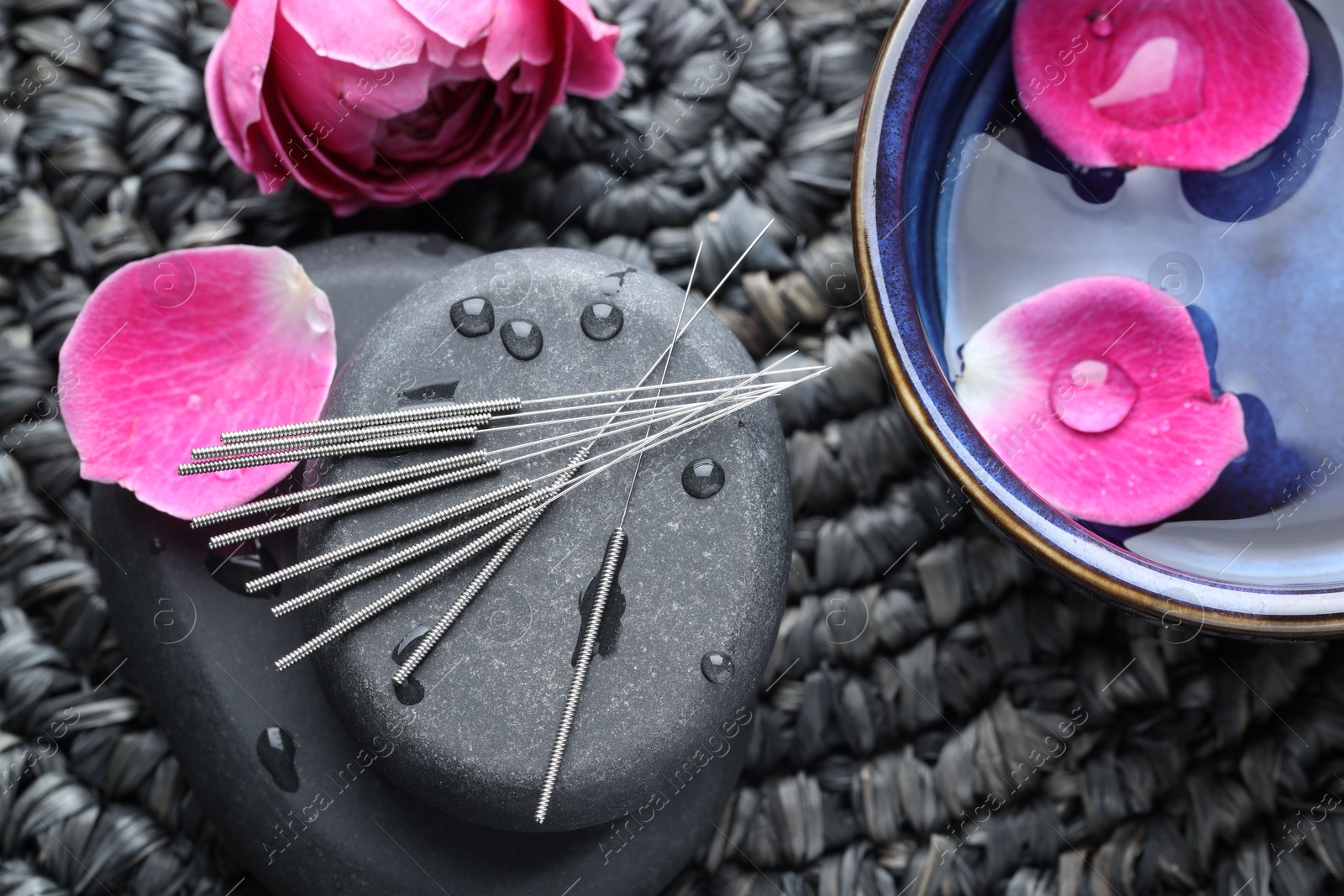 Acupuncture needles, wet spa stones and flowers on wicker mat, flat lay Photo of Acupuncture needles, wet spa stones and flowers on wicker mat, flat lay