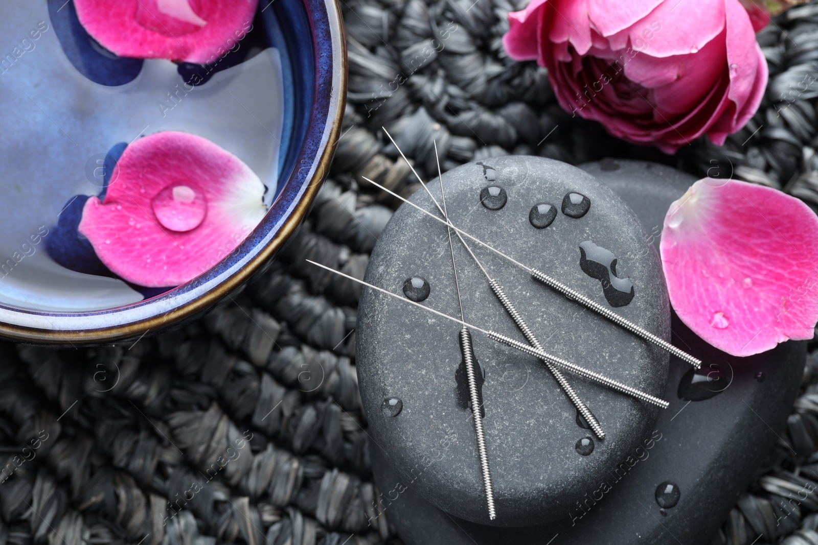 Acupuncture needles, wet spa stones and flowers on wicker mat, flat lay Photo of Acupuncture needles, wet spa stones and flowers on wicker mat, flat lay
