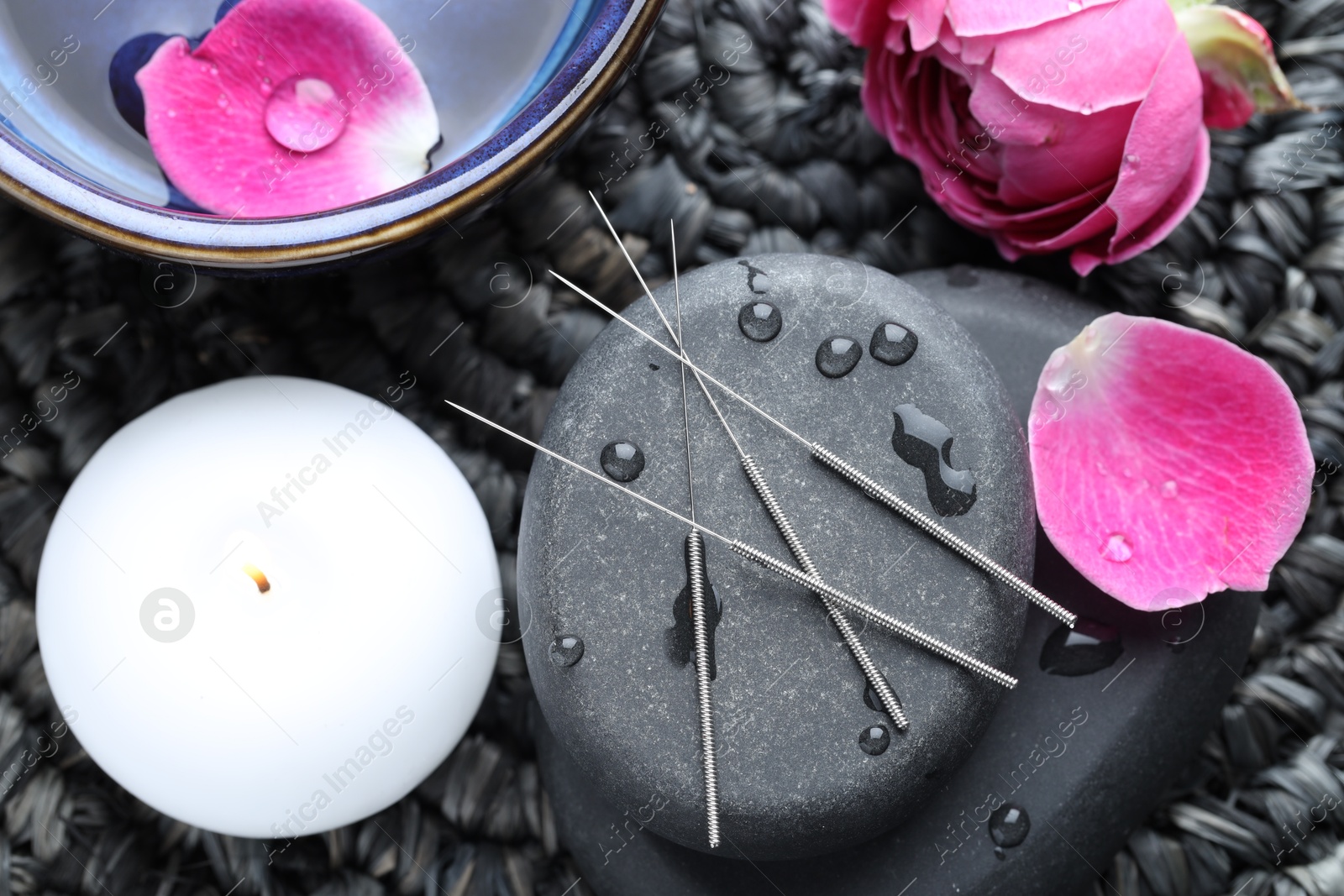 Acupuncture needles, wet spa stones, burning candle and flowers on wicker mat, flat lay Photo of Acupuncture needles, wet spa stones, burning candle and flowers on wicker mat, flat lay