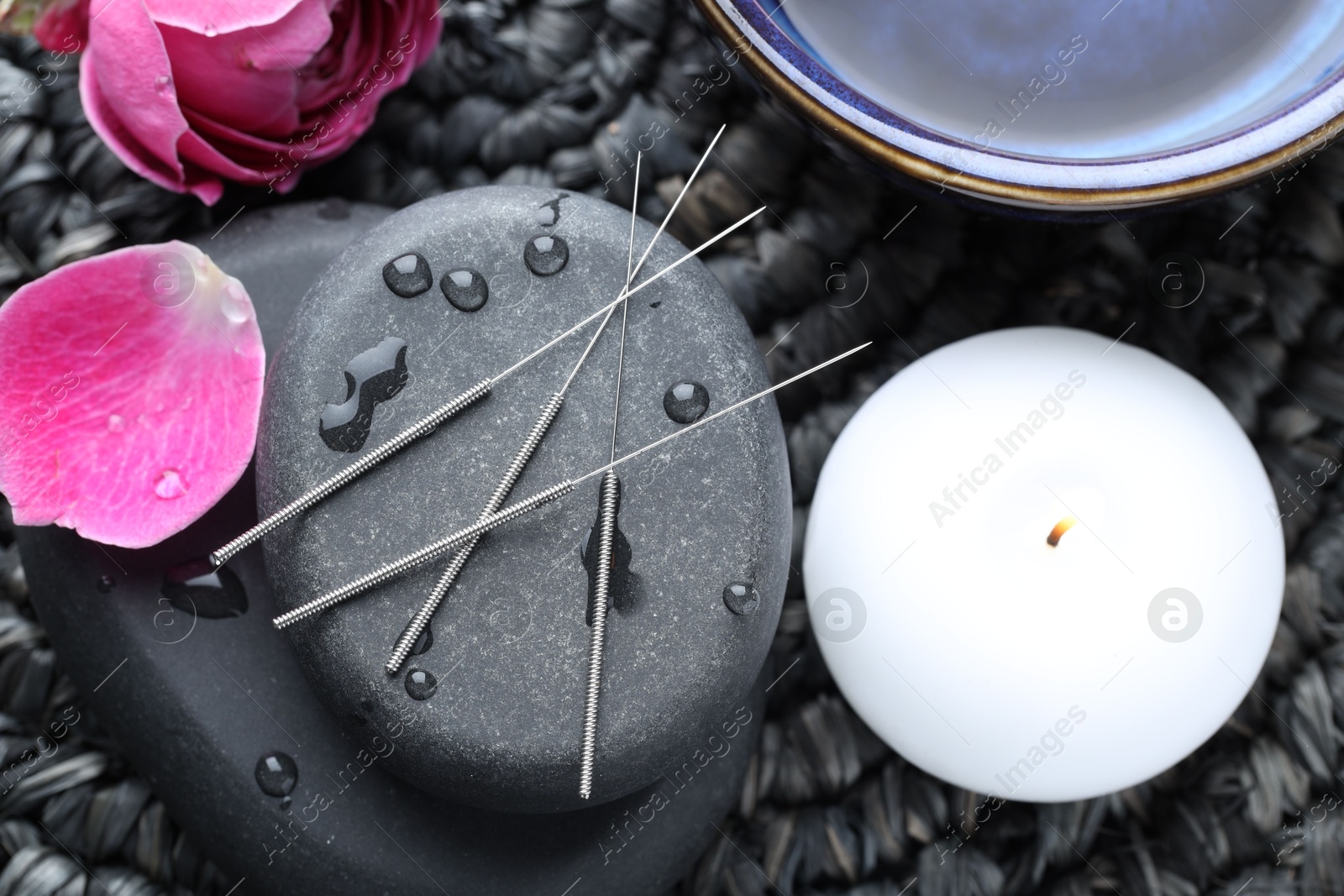 Acupuncture needles, wet spa stones, burning candle and flowers on wicker mat, flat lay Photo of Acupuncture needles, wet spa stones, burning candle and flowers on wicker mat, flat lay