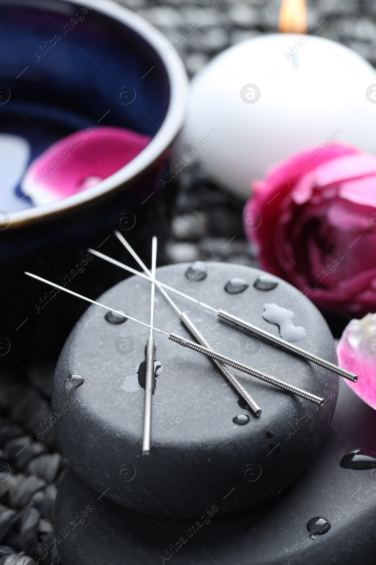 Acupuncture needles, wet spa stones, burning candle and flowers on wicker mat, closeup Photo of Acupuncture needles, wet spa stones, burning candle and flowers on wicker mat, closeup
