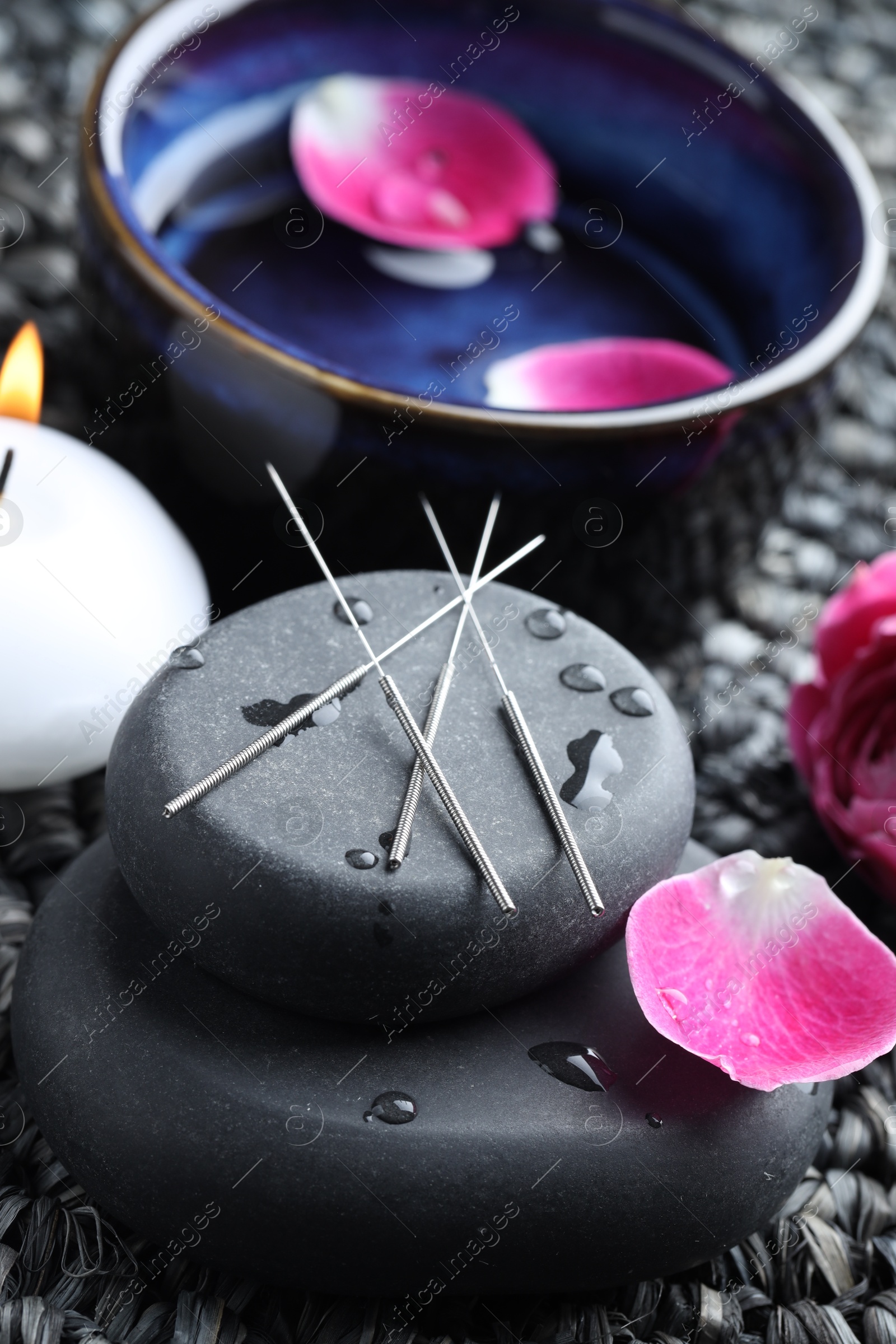 Acupuncture needles, wet spa stones, burning candle and flowers on wicker mat, closeup Photo of Acupuncture needles, wet spa stones, burning candle and flowers on wicker mat, closeup