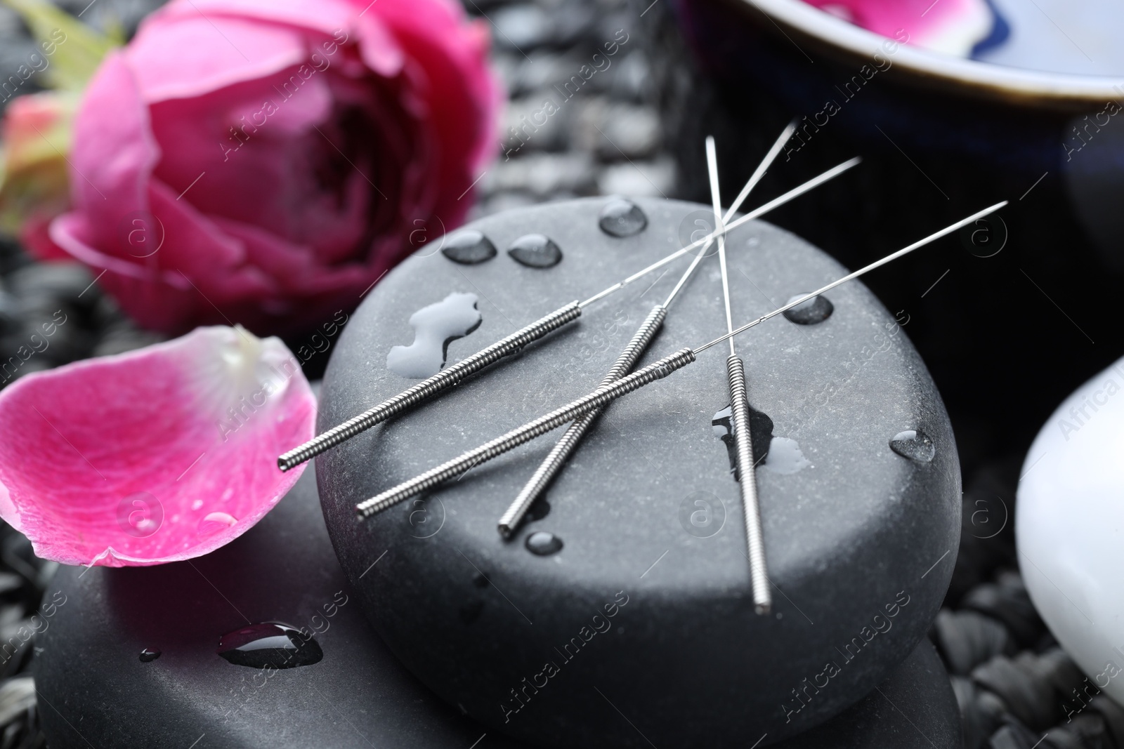 Acupuncture needles, wet spa stones and flowers on wicker mat, closeup Photo of Acupuncture needles, wet spa stones and flowers on wicker mat, closeup
