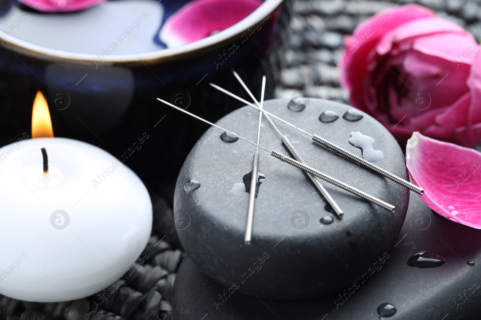 Acupuncture needles, wet spa stones, burning candle and flowers on wicker mat, closeup Photo of Acupuncture needles, wet spa stones, burning candle and flowers on wicker mat, closeup