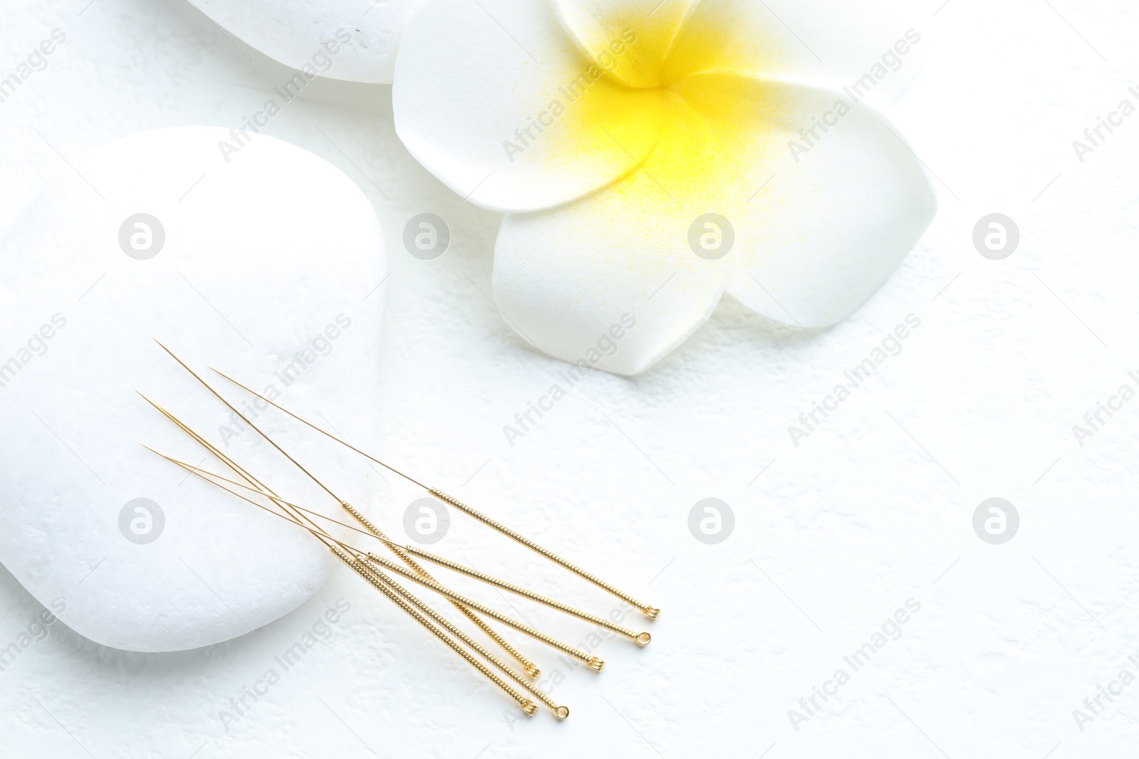 Acupuncture needles, spa stones and flower on white background, flat lay Photo of Acupuncture needles, spa stones and flower on white background, flat lay