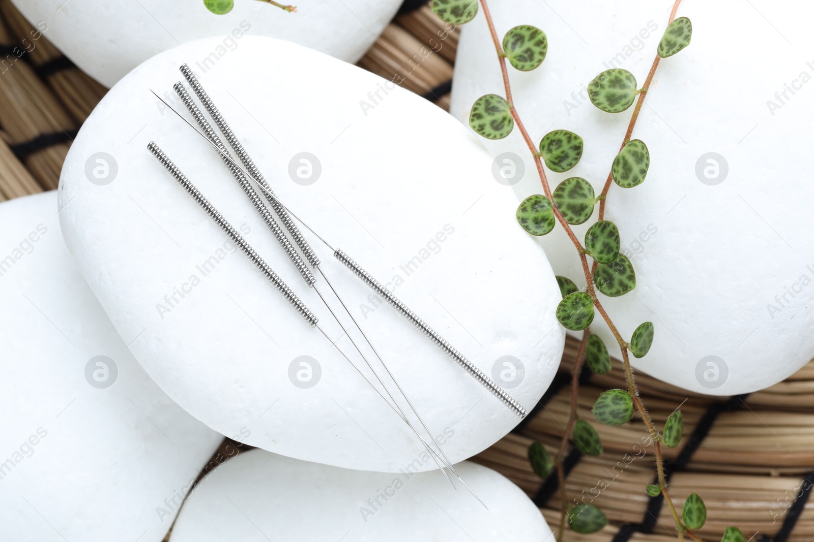 Acupuncture needles, spa stones and leaves on wicker mat, closeup Photo of Acupuncture needles, spa stones and leaves on wicker mat, closeup