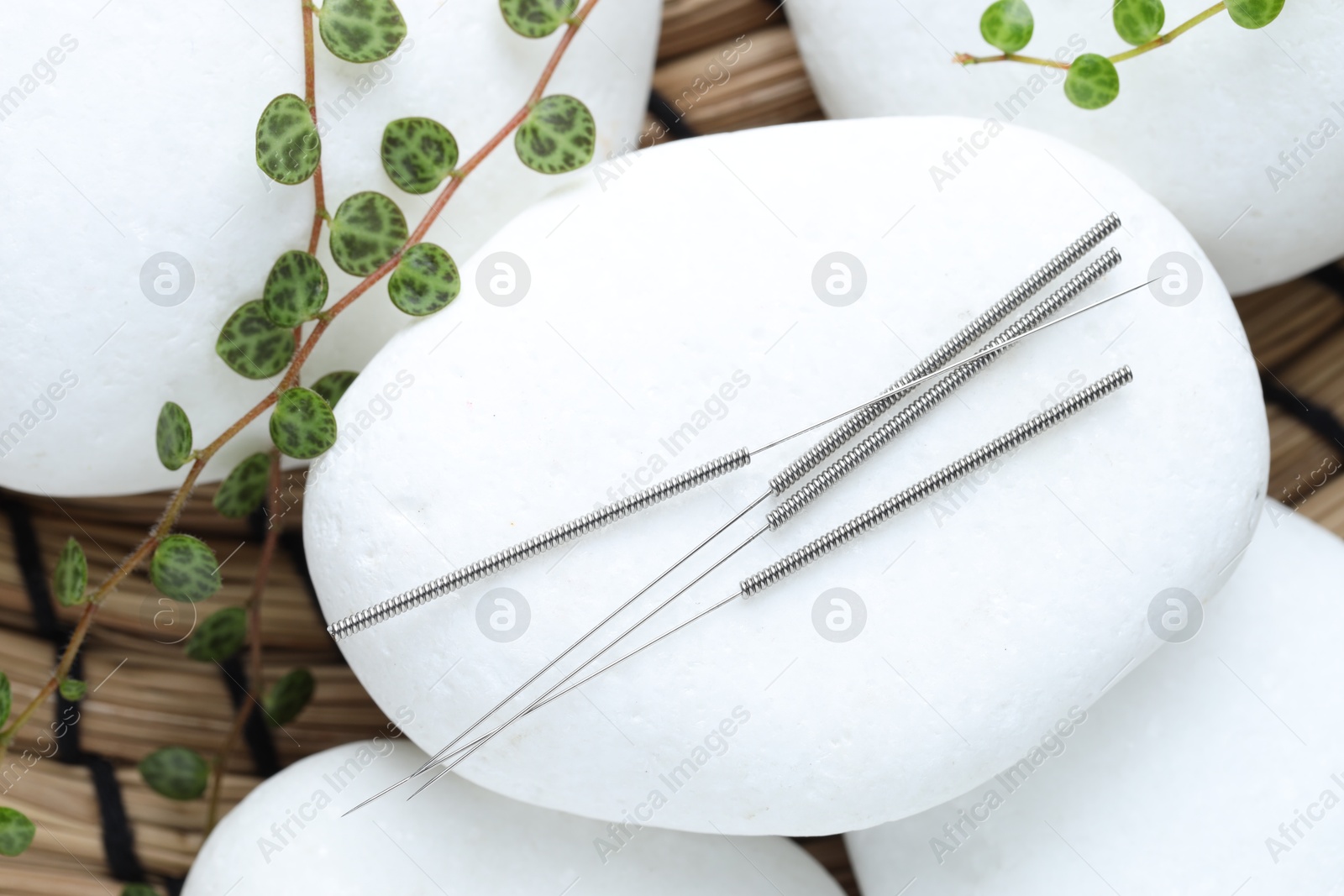 Acupuncture needles, spa stones and leaves on wicker mat, closeup Photo of Acupuncture needles, spa stones and leaves on wicker mat, closeup
