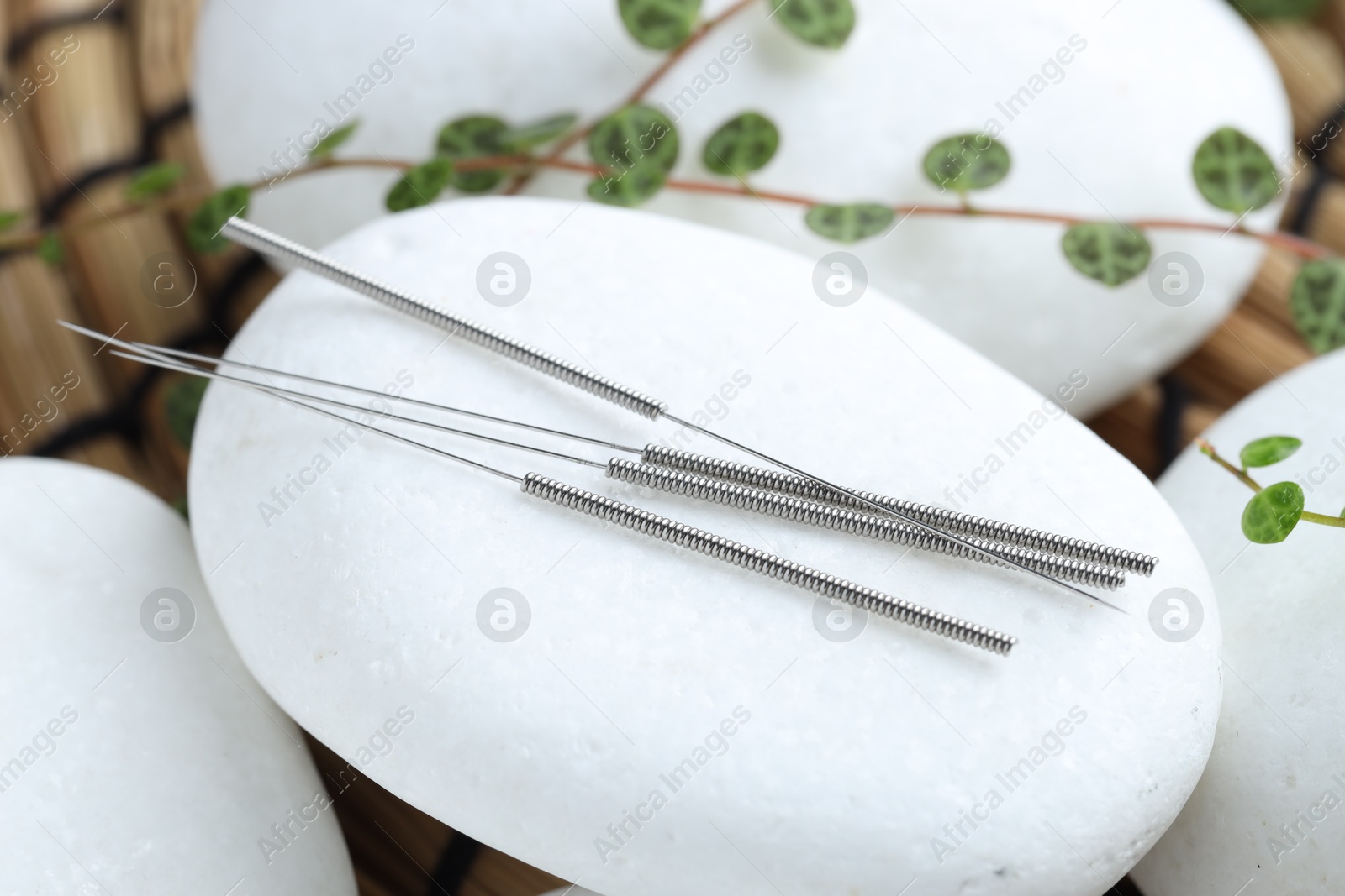 Acupuncture needles, spa stones and leaves on wicker mat, closeup Photo of Acupuncture needles, spa stones and leaves on wicker mat, closeup