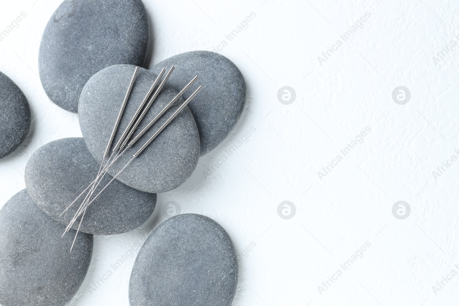 Acupuncture needles and spa stones on white background, flat lay. Space for text Photo of Acupuncture needles and spa stones on white background, flat lay. Space for text