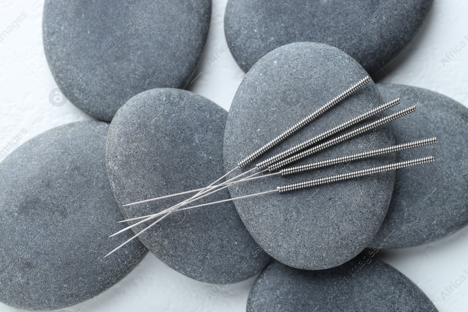 Acupuncture needles and spa stones on white background, flat lay Photo of Acupuncture needles and spa stones on white background, flat lay