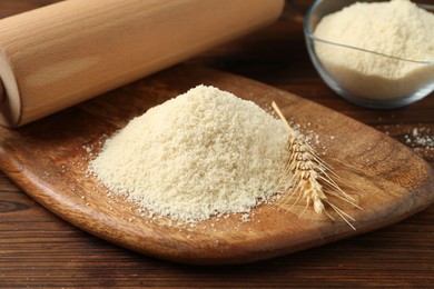 Photo of Pile of flour, spike and rolling pin on wooden table, closeup