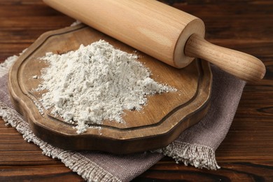 Photo of Pile of flour and rolling pin on wooden table, closeup