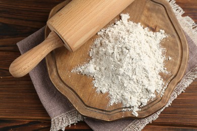 Photo of Pile of flour and rolling pin on wooden table, top view