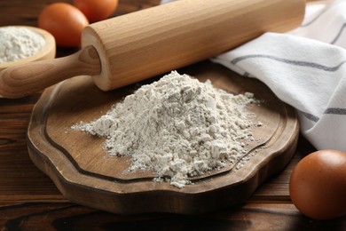 Photo of Pile of flour, eggs and rolling pin on wooden table, closeup