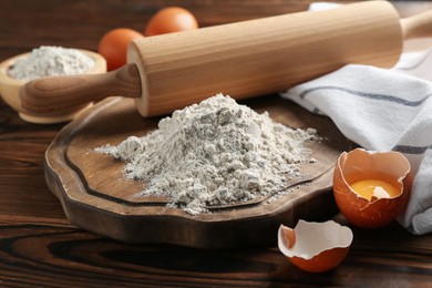 Photo of Pile of flour, eggs and rolling pin on wooden table, closeup