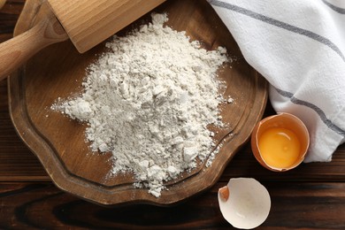 Photo of Pile of flour, egg and rolling pin on wooden table, flat lay