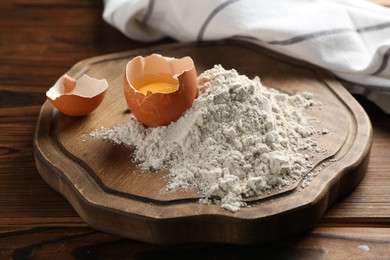 Photo of Pile of flour and egg on wooden table, closeup