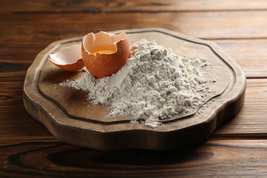 Photo of Pile of flour and egg on wooden table, closeup