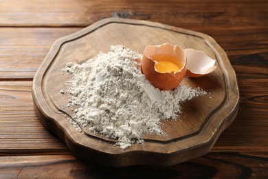 Photo of Pile of flour and egg on wooden table, closeup
