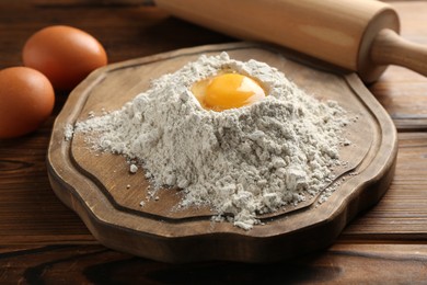 Photo of Pile of flour, eggs and rolling pin on wooden table, closeup
