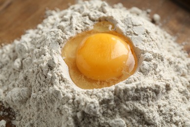 Photo of Pile of flour and egg on wooden table, closeup