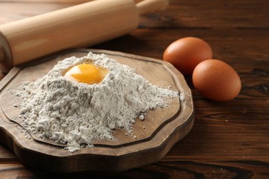 Photo of Pile of flour, eggs and rolling pin on wooden table, closeup