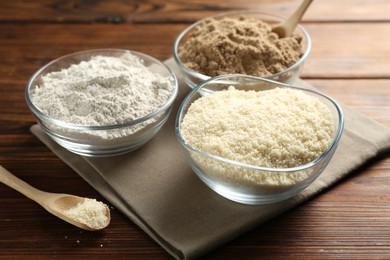 Photo of Different types of flour in bowls on wooden table, closeup