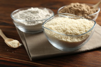 Photo of Different types of flour in bowls on wooden table, closeup