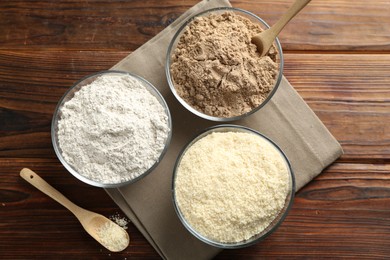 Photo of Different types of flour in bowls on wooden table, top view