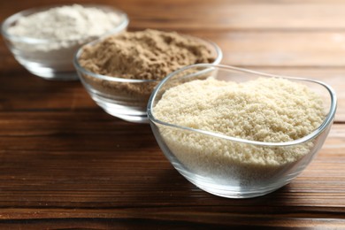 Photo of Different types of flour in bowls on wooden table, closeup